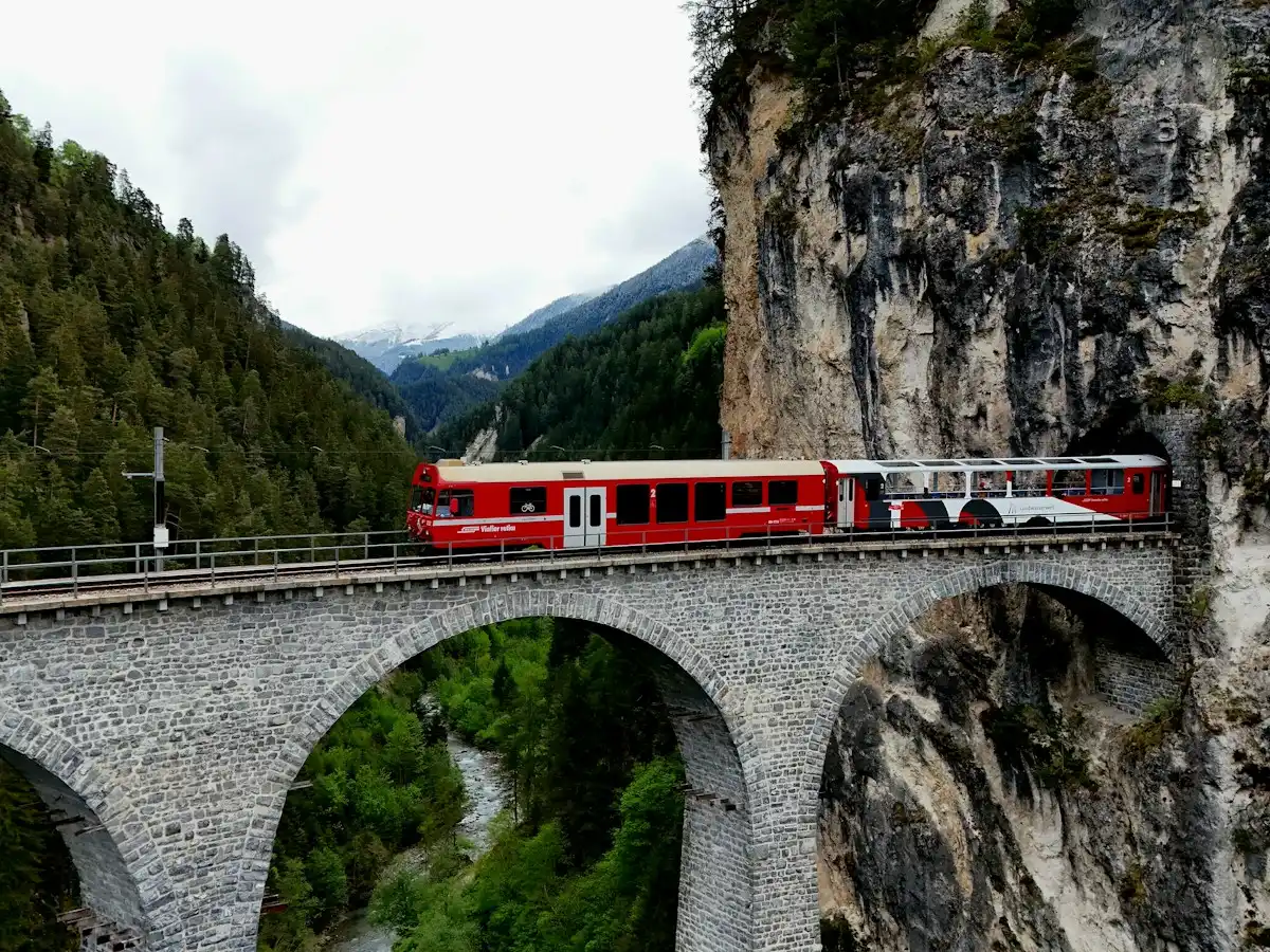 Red train crosses a stone bridge in a mountain valley — Landwasser Viaduct, Switzerland
